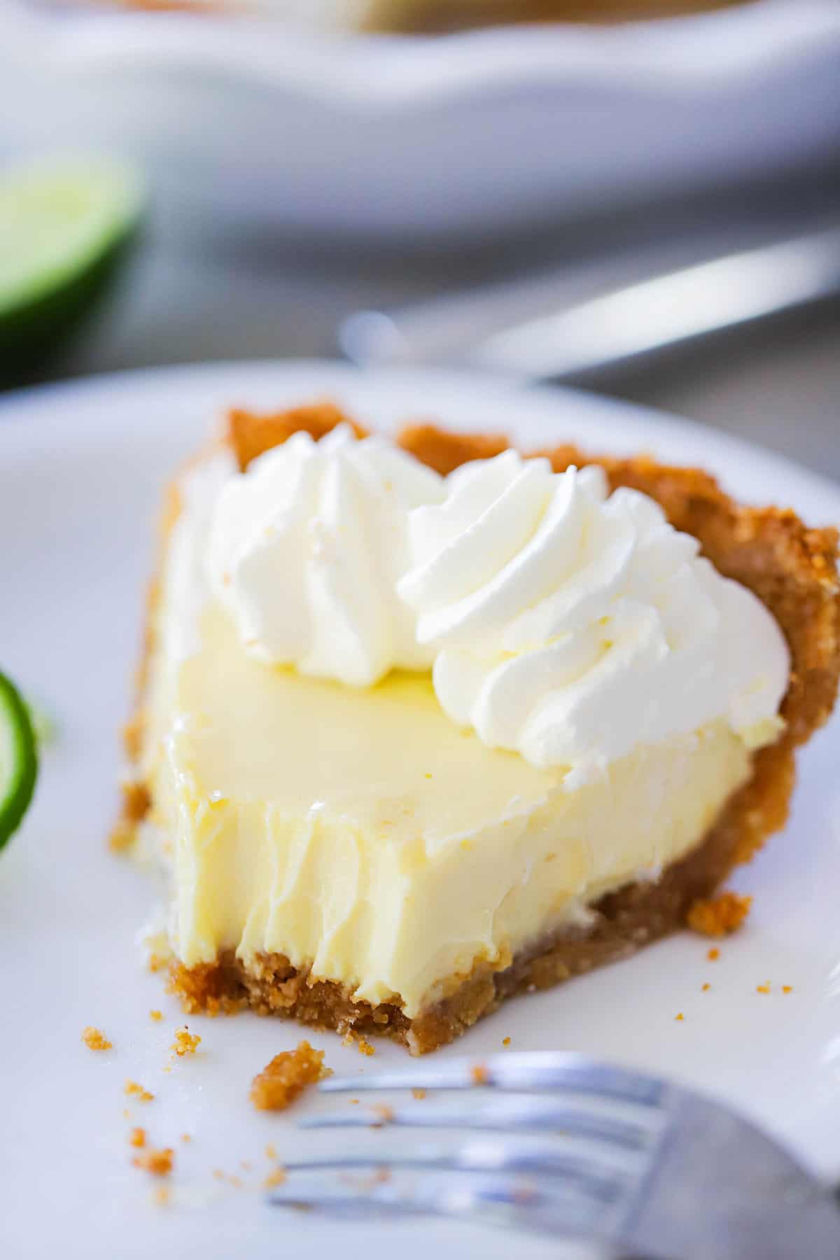 A partially eaten key lime pie on a white dessert plate with a fork resting nearby. 