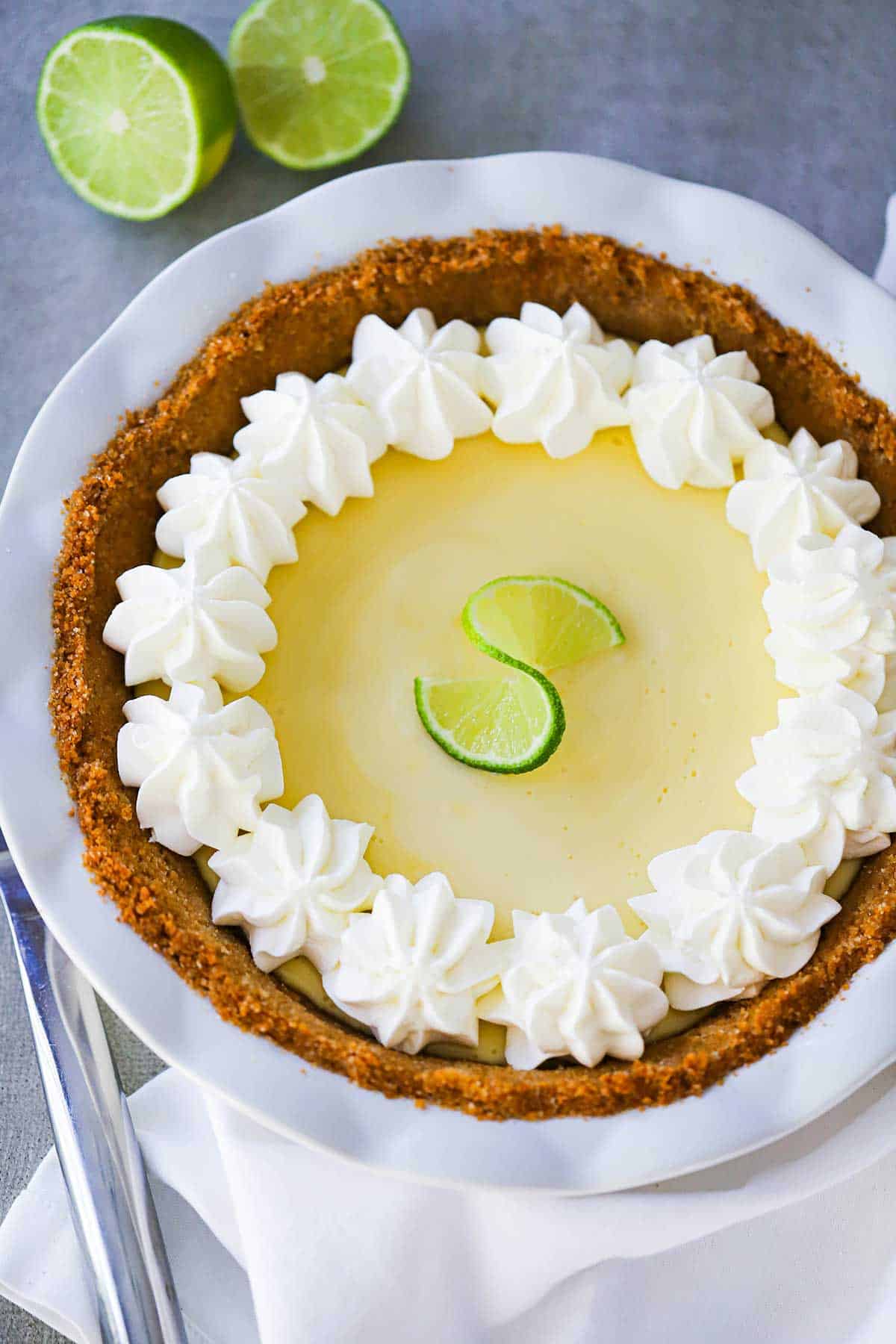 A key lime pie with a graham cracker crust and whipped cream pinwheels along the edges of the top of the pie. 