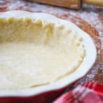 Easy pie crust dough that has been fitted into a ceramic pie dish with a floured rolling pin nearby.