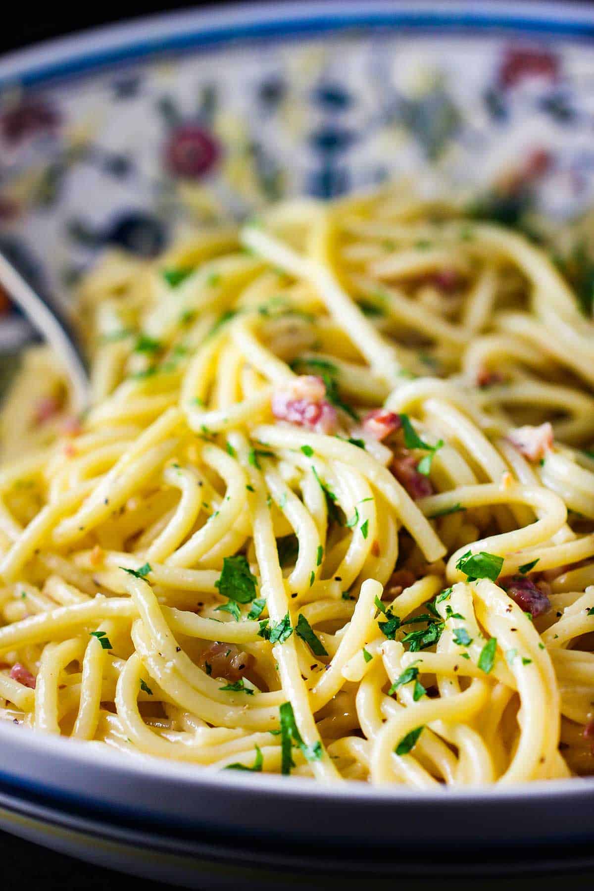A large colorful pasta bowl filled with creamy pasta carbonara. 