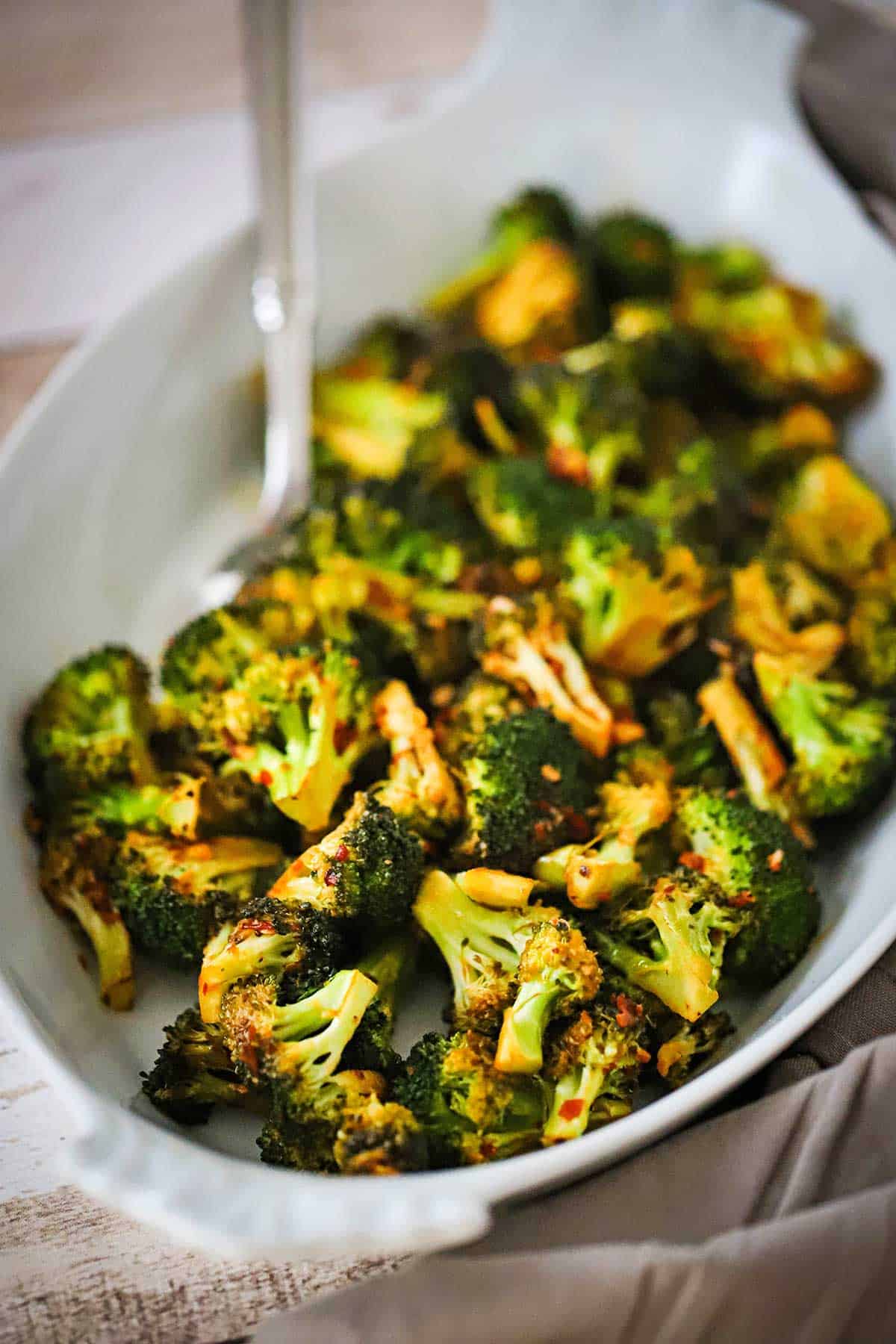 An oval baking dish filled with roasted broccoli with kick and a spoon inserted into the dish. 