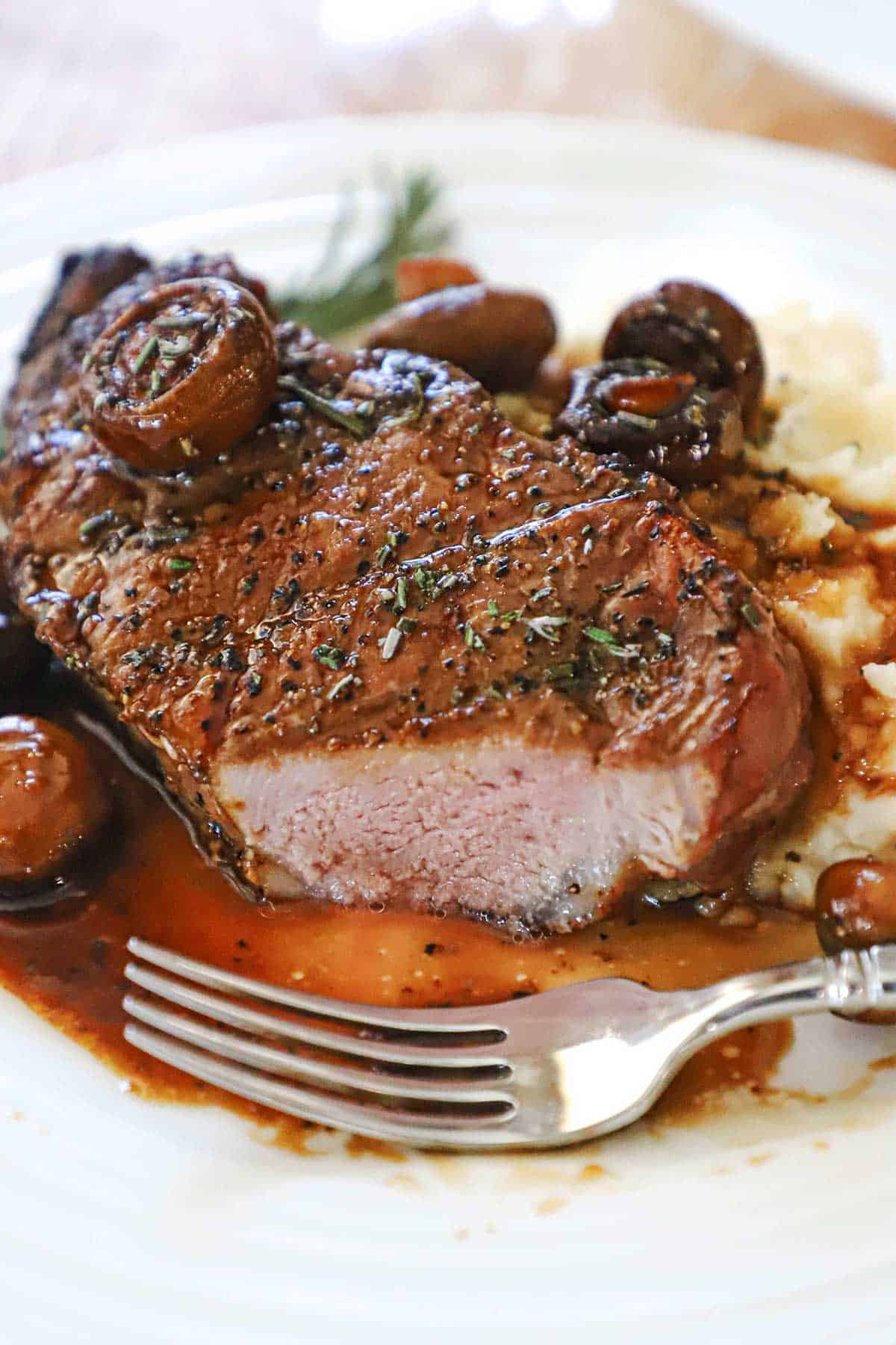 A partially eaten pork chop agrodolce with mushrooms sitting on a white dinner plate. 