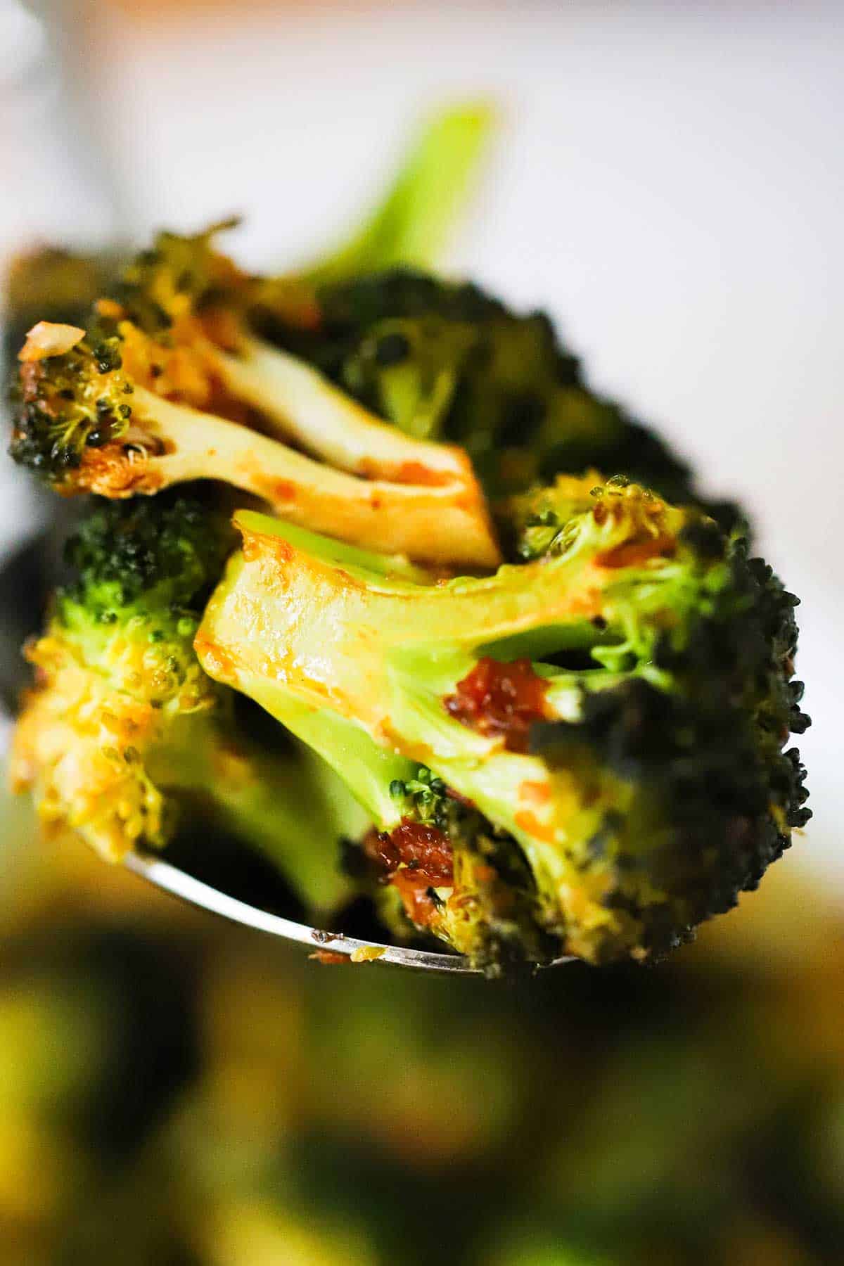 A large serving spoon holding up a serving of roasted broccoli with a kick. 