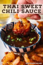 A person holding a crispy coconut shrimp by the tail and plunging the rest of it into a bowl of Thai sweet chili sauce.