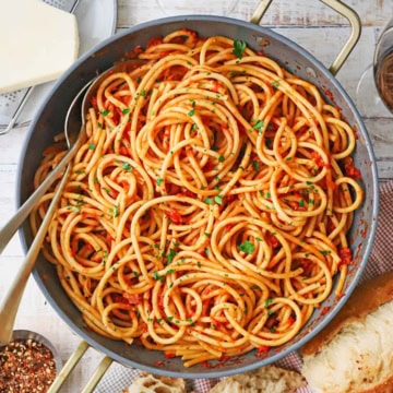A large, deep skillet filled with Bucatini all’Amatriciana with a block of cheese nearby.