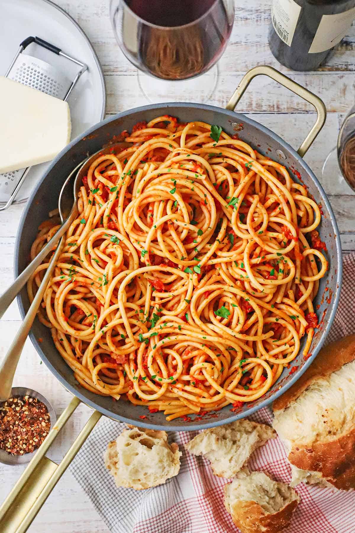 A large, deep skillet filled with Bucatini all’Amatriciana with a block of cheese nearby. 