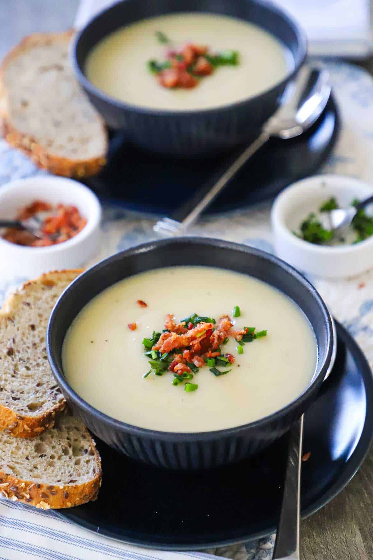 Two soup bowls filled with creamy Irish potato soup topped with crumbled bacon and snipped chives. 