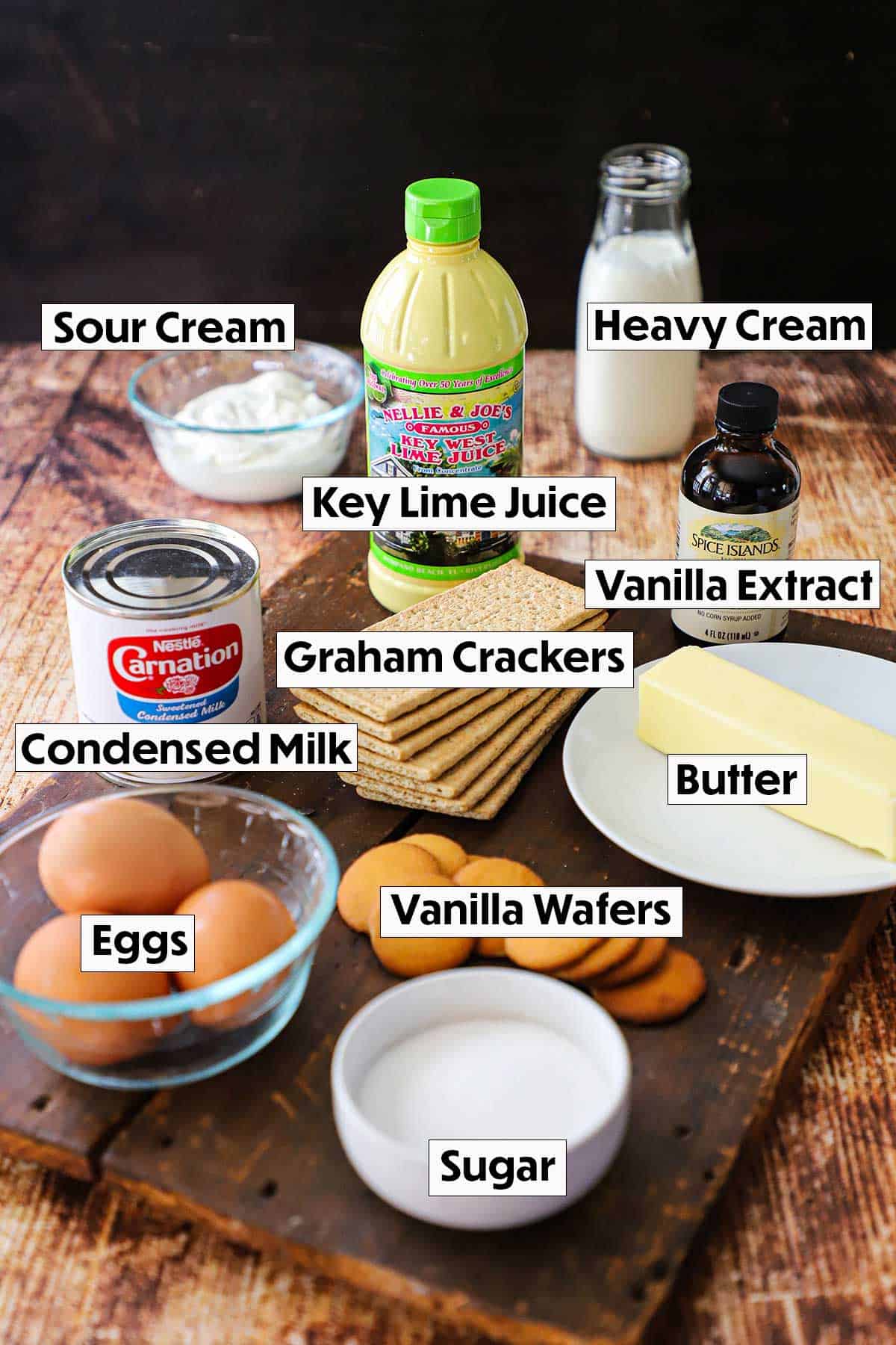 A collection of ingredients for Key Lime Pie arranged on a rustic wooden cutting board, including key limes juice, graham crackers, sweetened condensed milk, and eggs, showcasing their vibrant colors and textures.