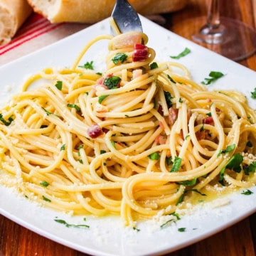 A plate of pasta carbonara with a fork in the center of the pasta that is twirling the noodles.