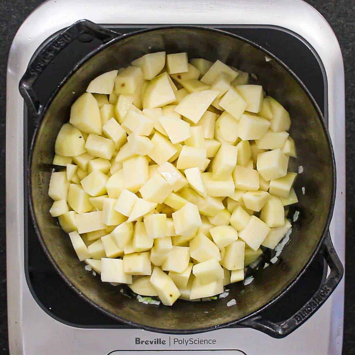 Peeled and cubed Russet potatoes being sautéed in a large black pot.  