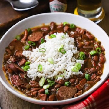 A straight-on view of a serving of red beans and rice in a white bowl and is garnished with chopped scallions.