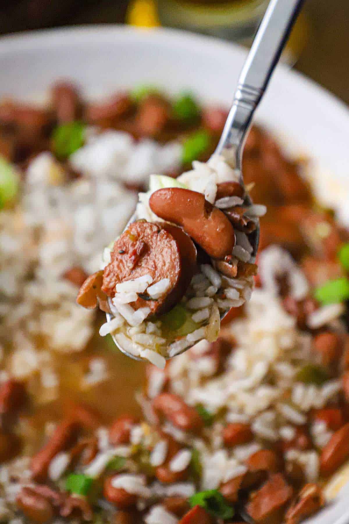 A close-up view of a silver spoon holding up a spoonful of red beans and rice over a bowl filled with the same.