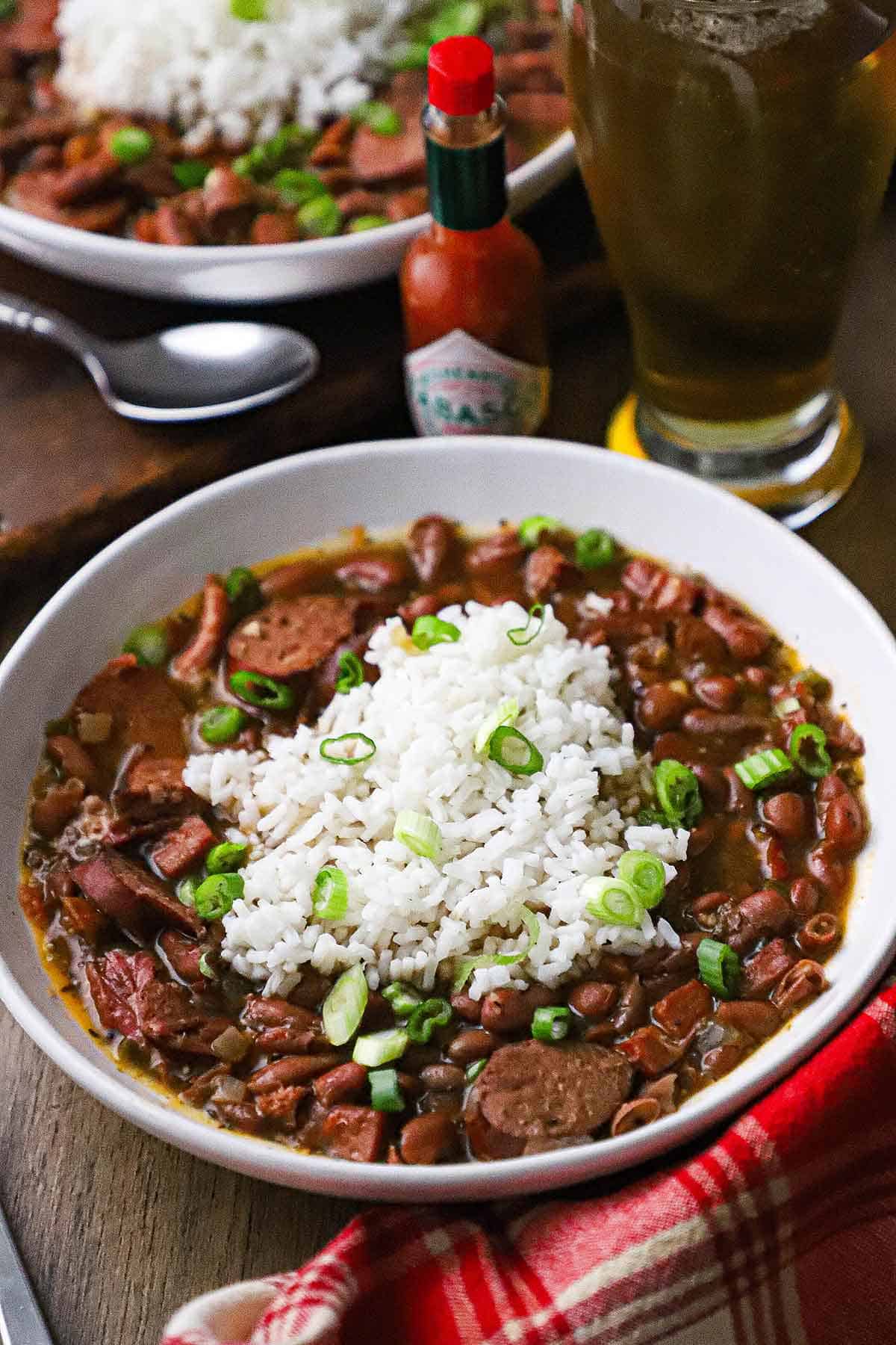 A straight-on view of a white bowl filled with a serving of red beans and rice with chunks of andouille sausage and smoked ham visible.