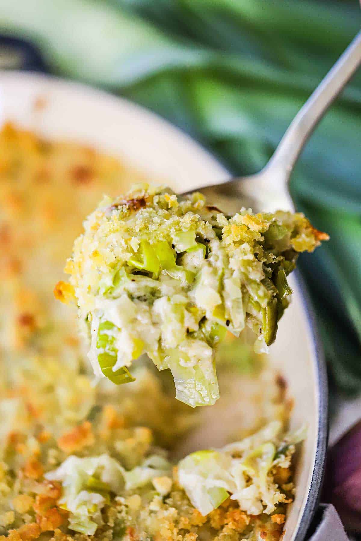 A person raising a silver spoon filled with a serving of baked leek gratin. 