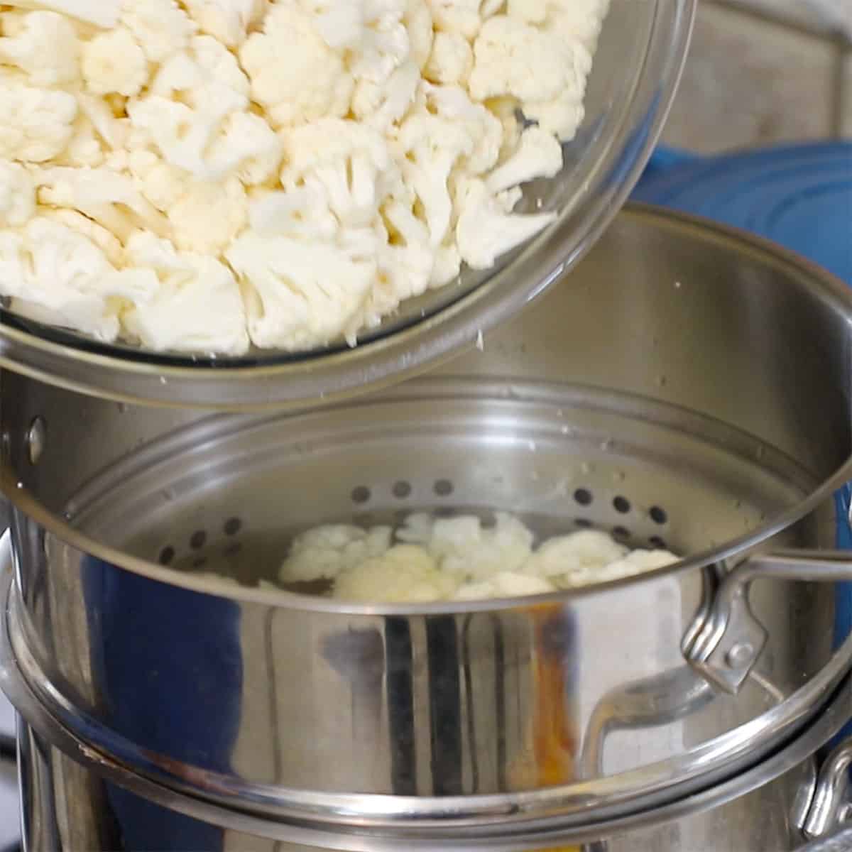 Cauliflower florets being adding to a pot of boiling water from a glass bowl. 