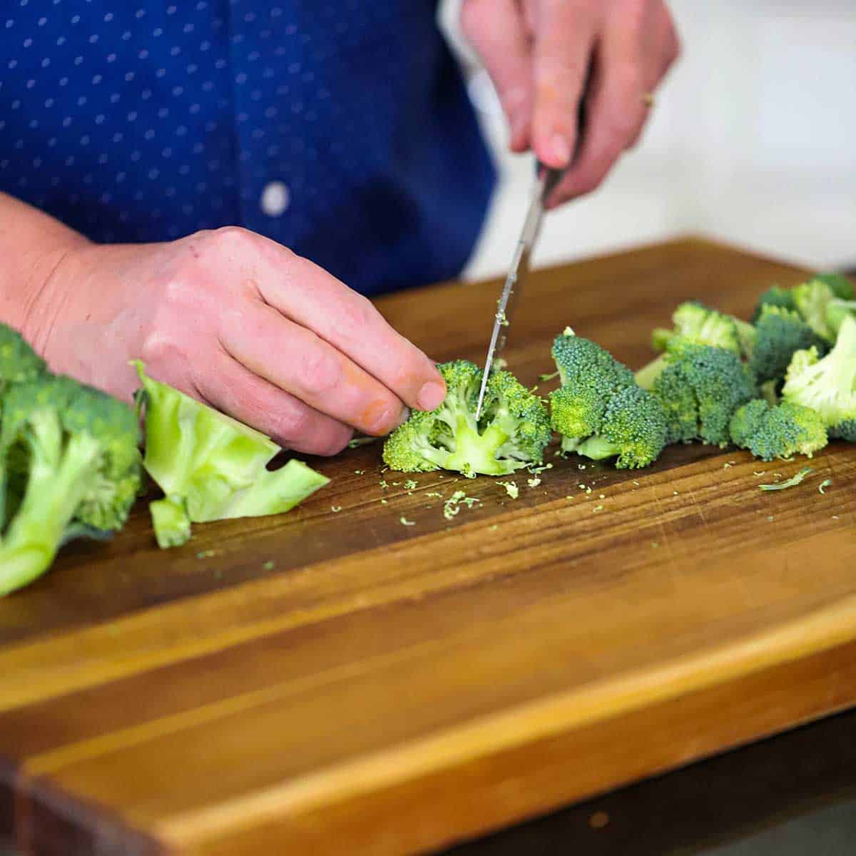 A person using a chef's knife to cut a head of broccoli into small florets. 