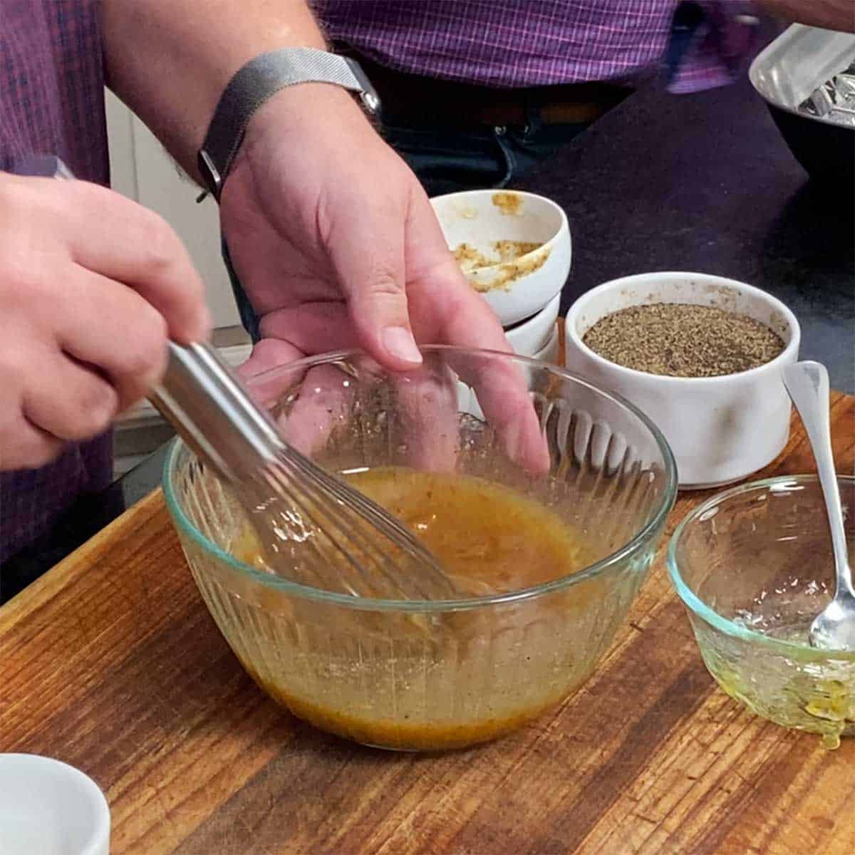 A person using a whisk to combine a glaze of bourbon, orange marmalade, mustard, and maple syrup. 