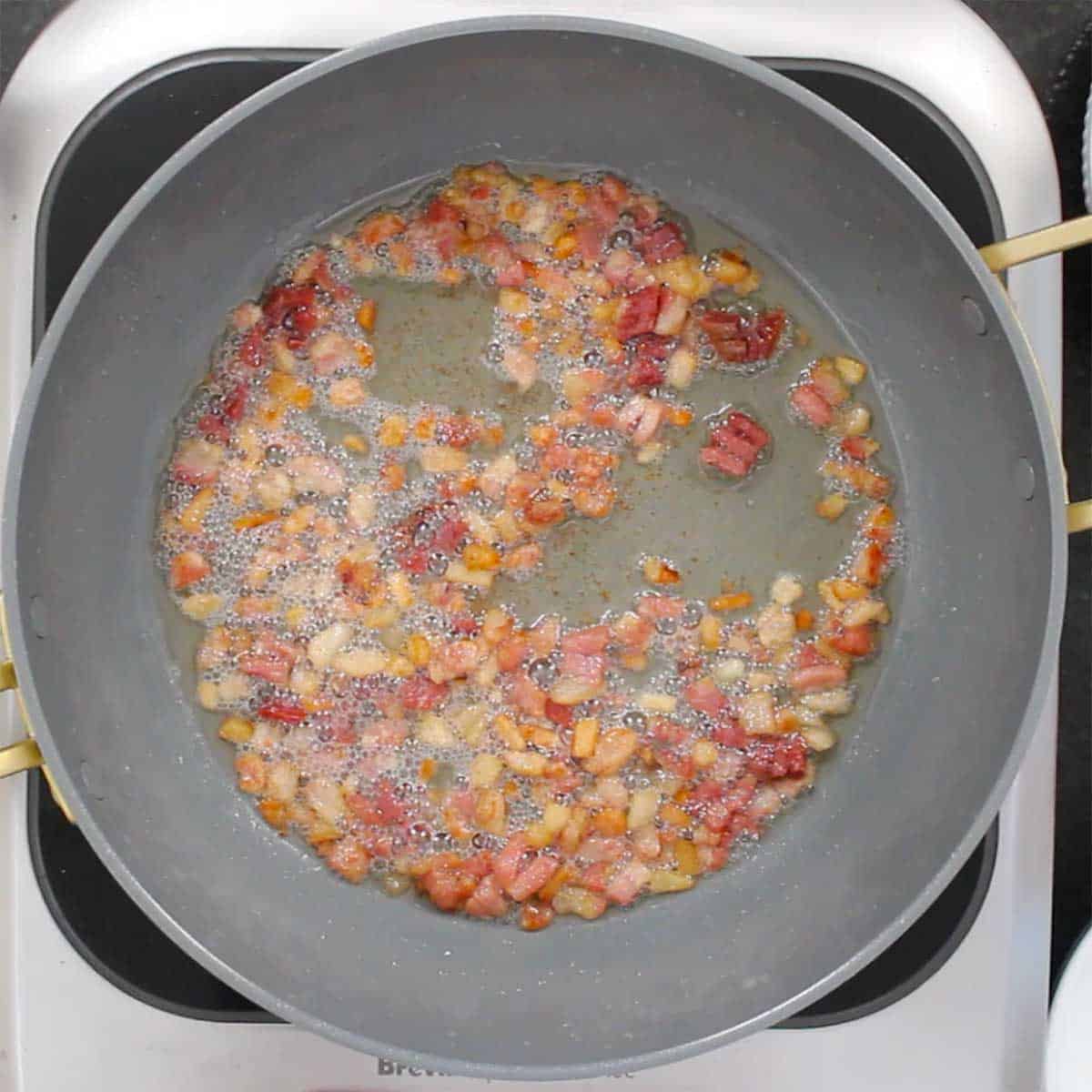 Cubed guanciale being sautéed in a large skillet on a portable induction stove. 