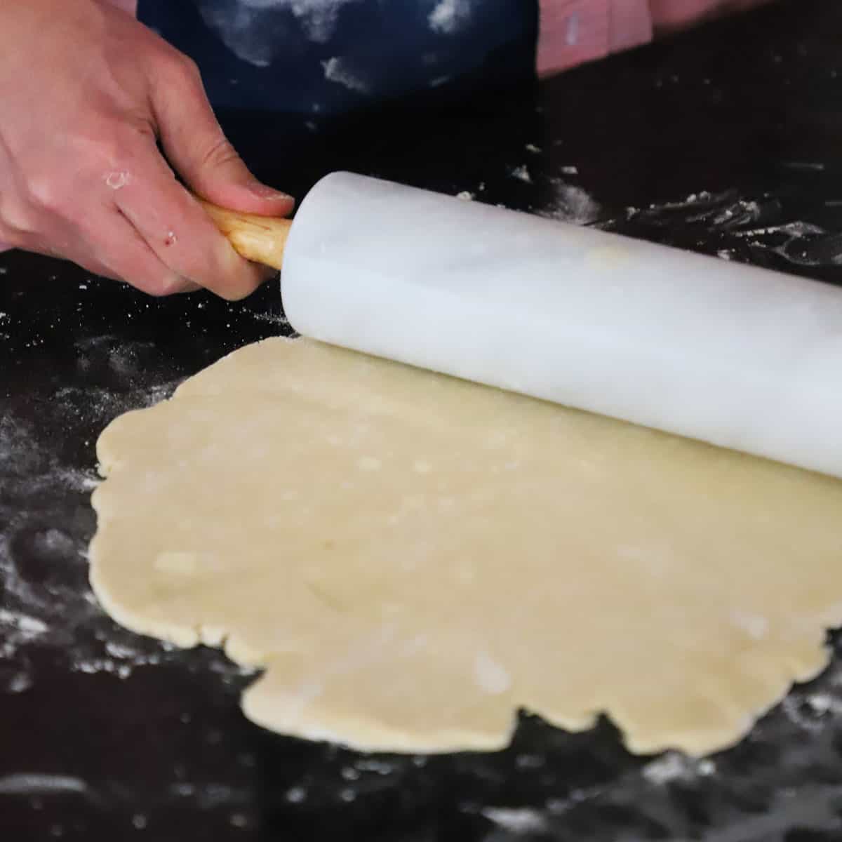 A person using a marble rolling pin to roll out pie dough for a pie crust. 