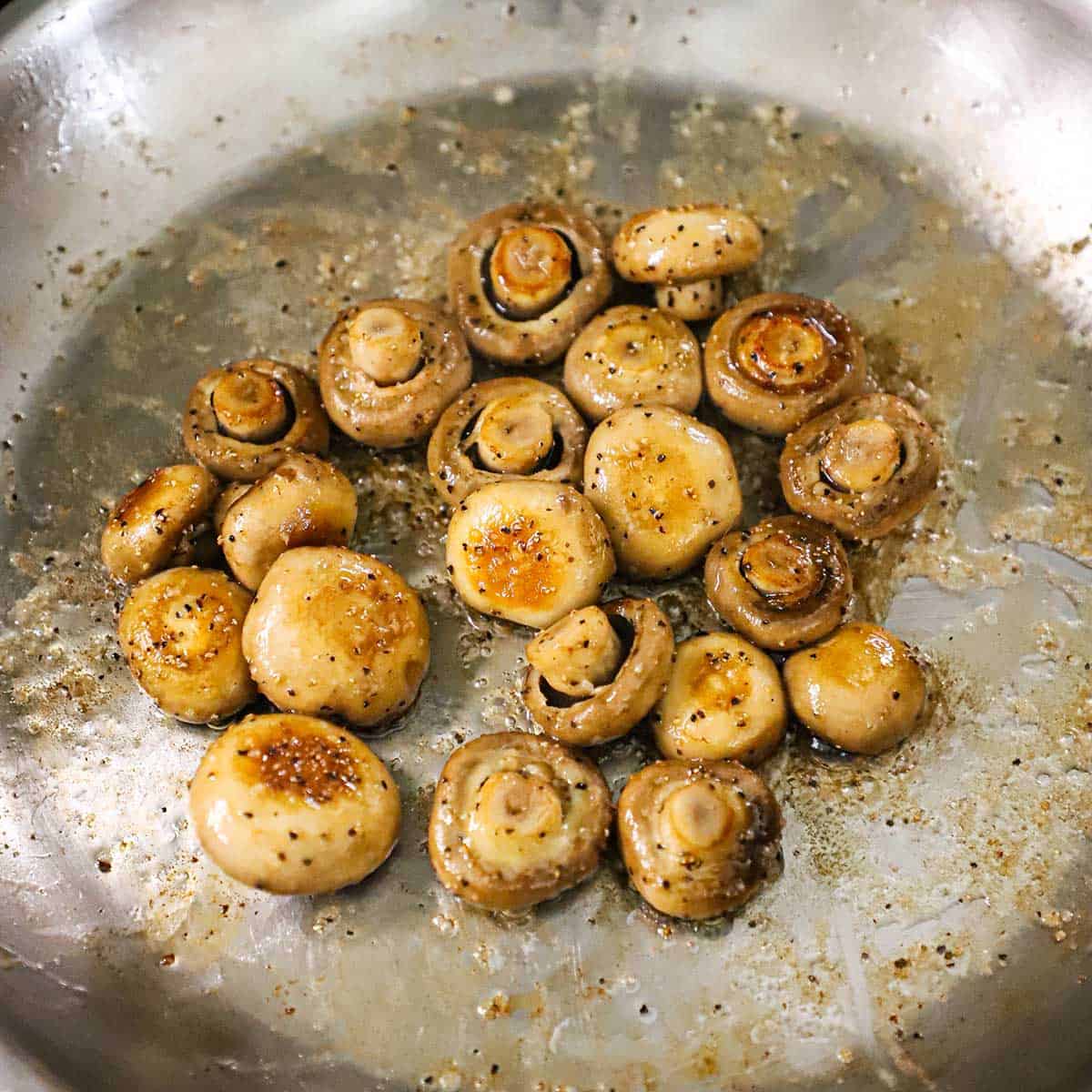 Whole button mushrooms in a large skillet that have been sautéed. 