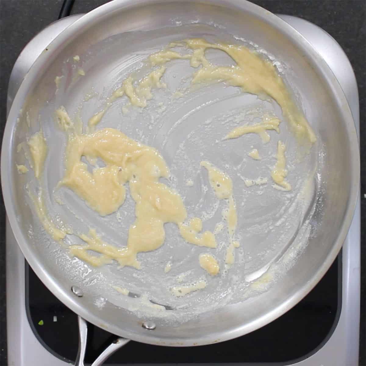 A roux being cooked in a large silver skillet on a hot plate. 