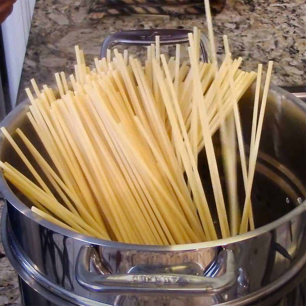 Dried pasta standing upright in a pasta pot filled with boiling water.