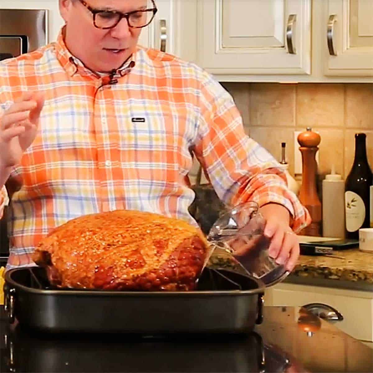 A man in an orange dress shirt looking down at a Berkshire ham that is resting in a large roasting pan. 