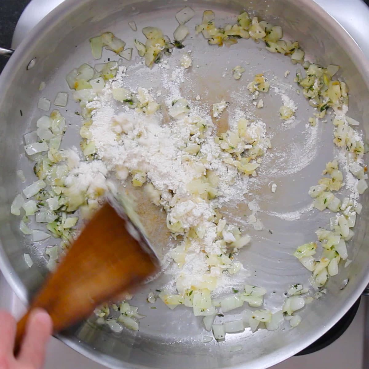 Sautéed onions with fresh thyme being combined with flour in a skillet to create a roux. 