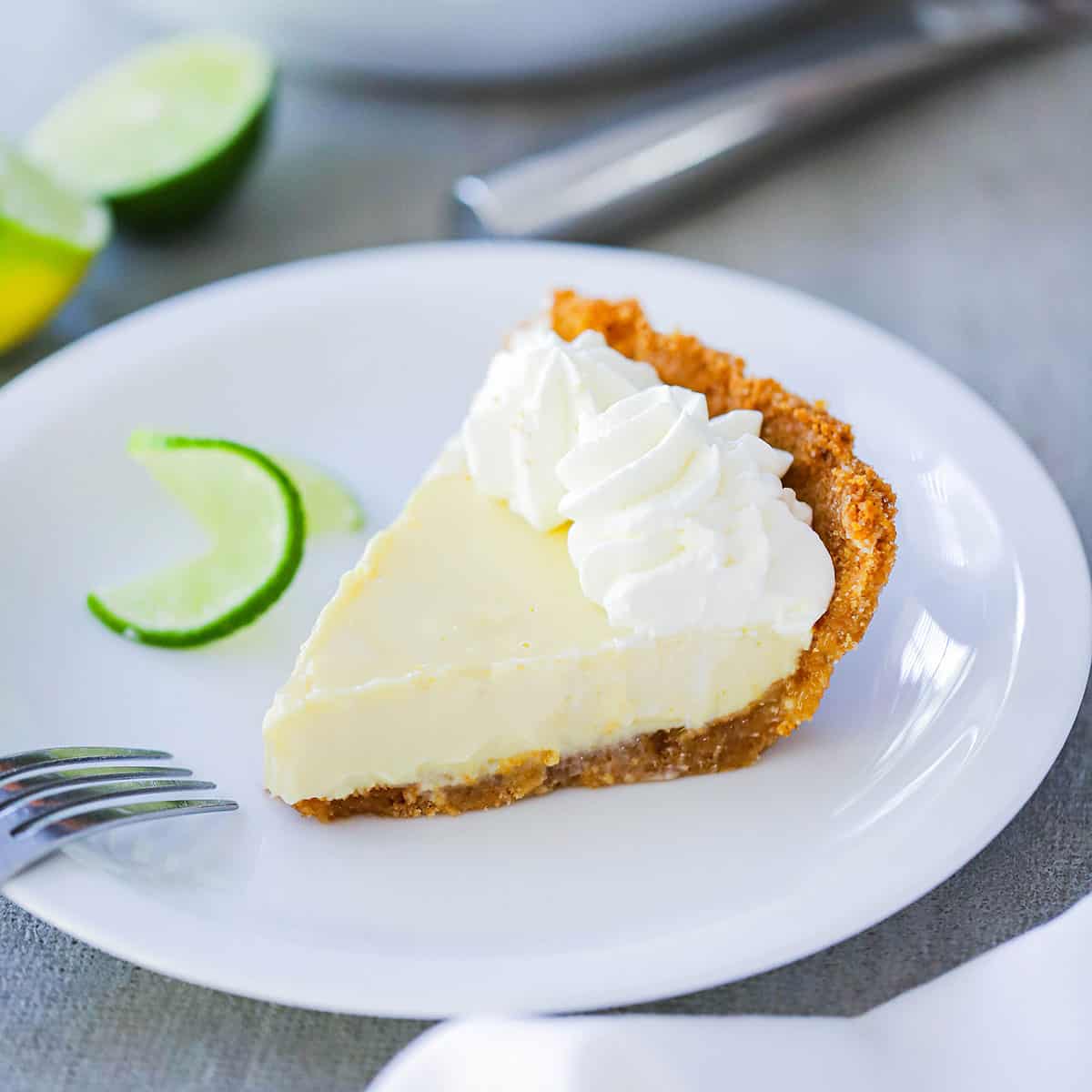 A slice of easy key lime pie resting on a white dessert plate with a fork nearby. 