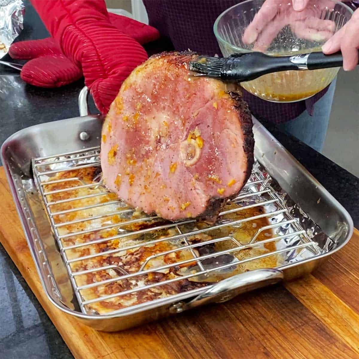 A person brushing on bourbon orange glaze onto a partially baked smoked ham. 