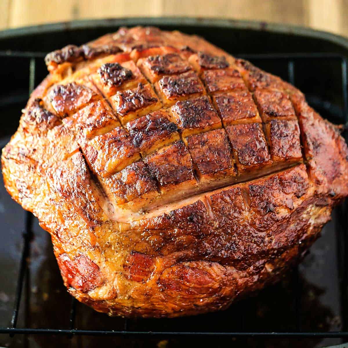 A fully cooked Berkshire ham that has been browned on top is resting in a large roasting pan. 