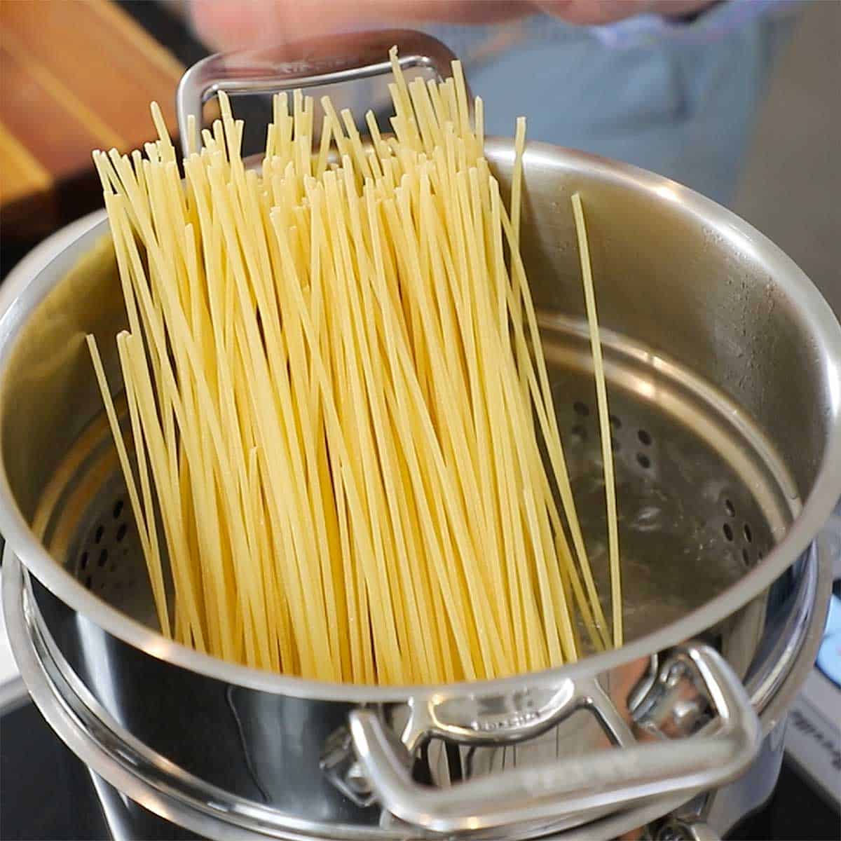 Dried spaghetti standing upright in pasta pot filled with boiling water. 