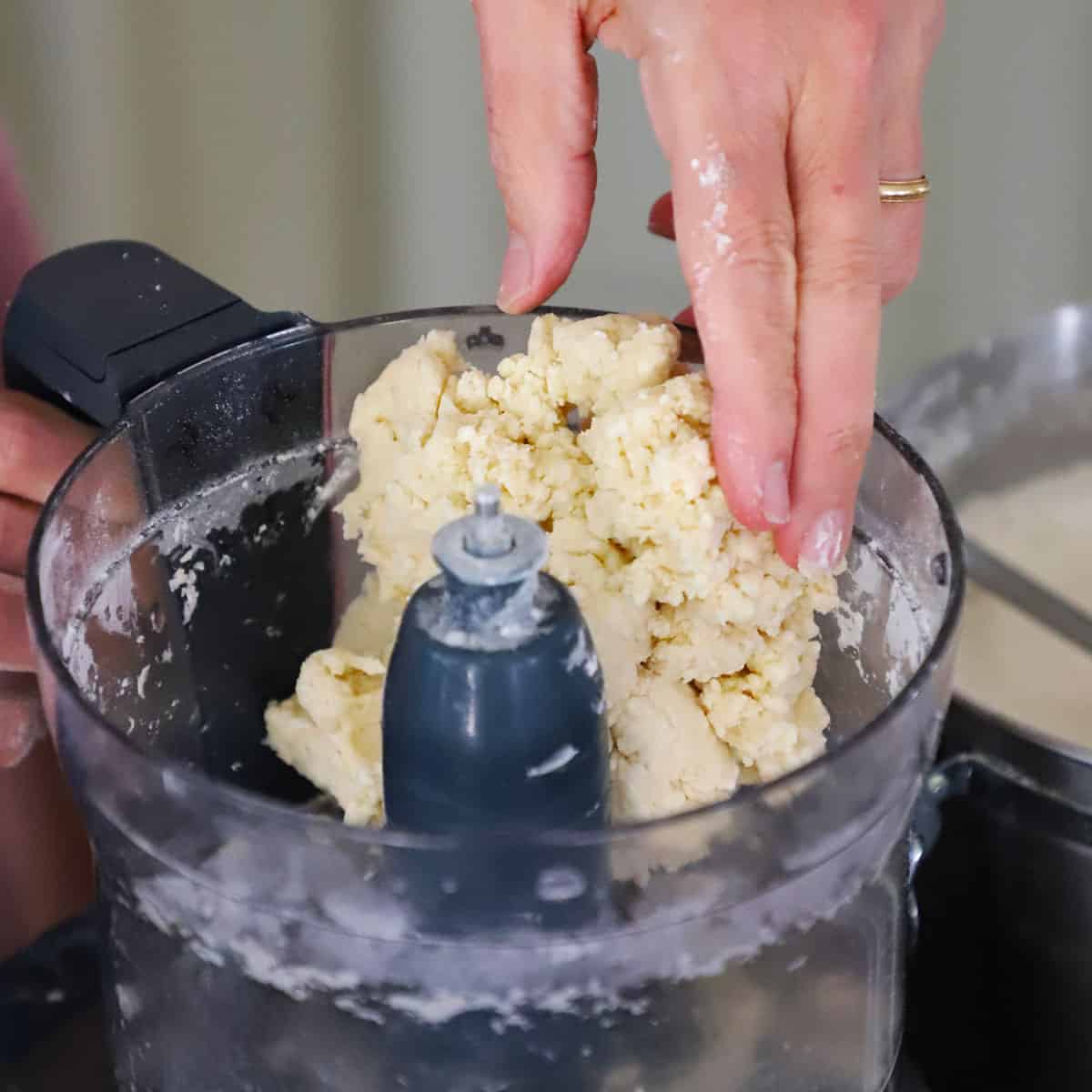 A person pulling a mass of pie dough from the base of a food processor. 