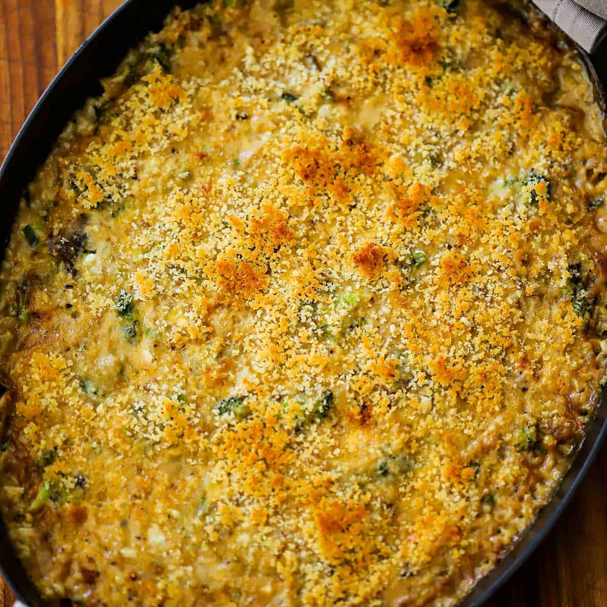 A baked broccoli casserole with cheddar and rice in an oval baking dish sitting on a wooden cutting board. 
