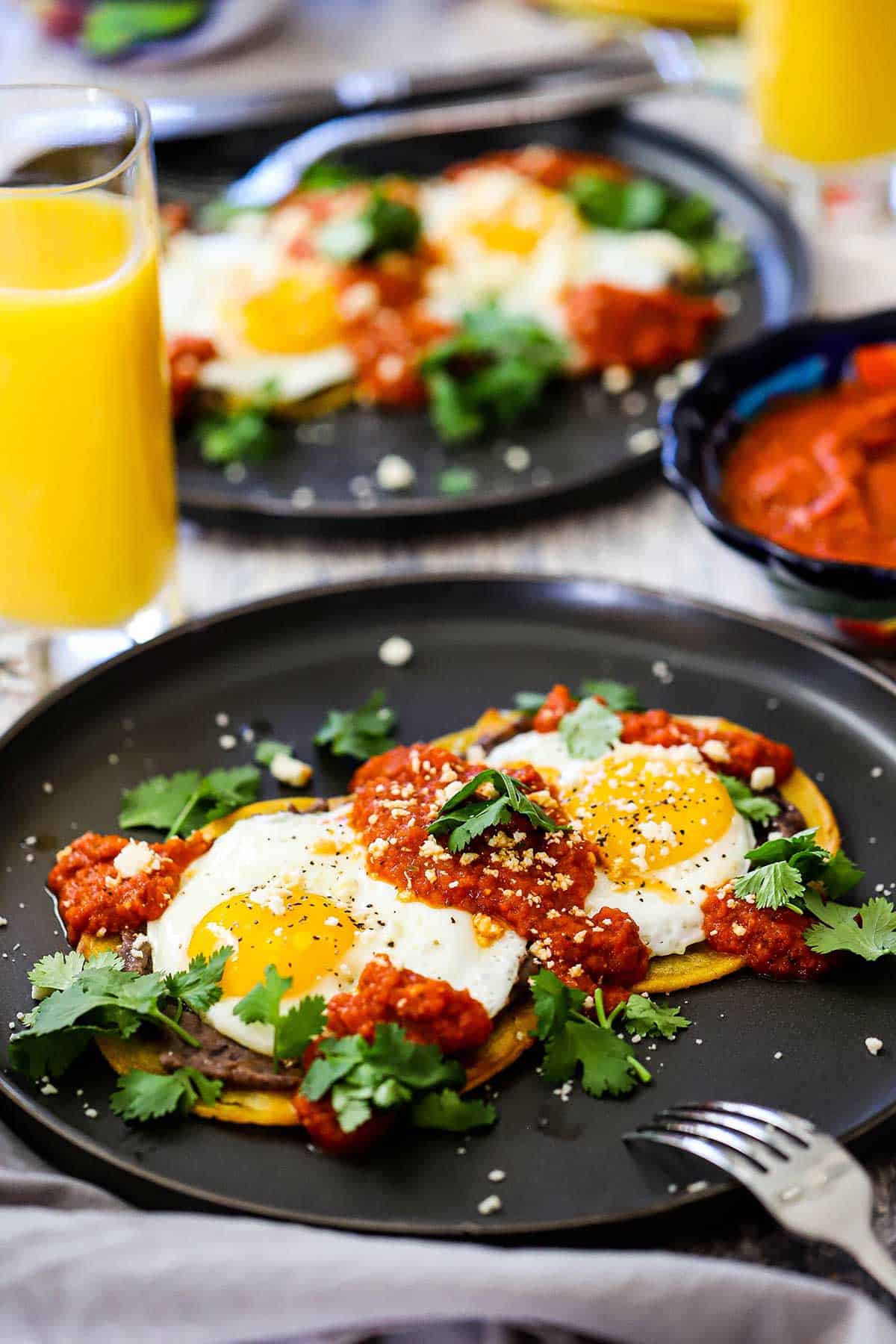 A serving of huevos rancheros on a black plate garnished with crumbled Cotija cheese and chopped fresh cilantro.