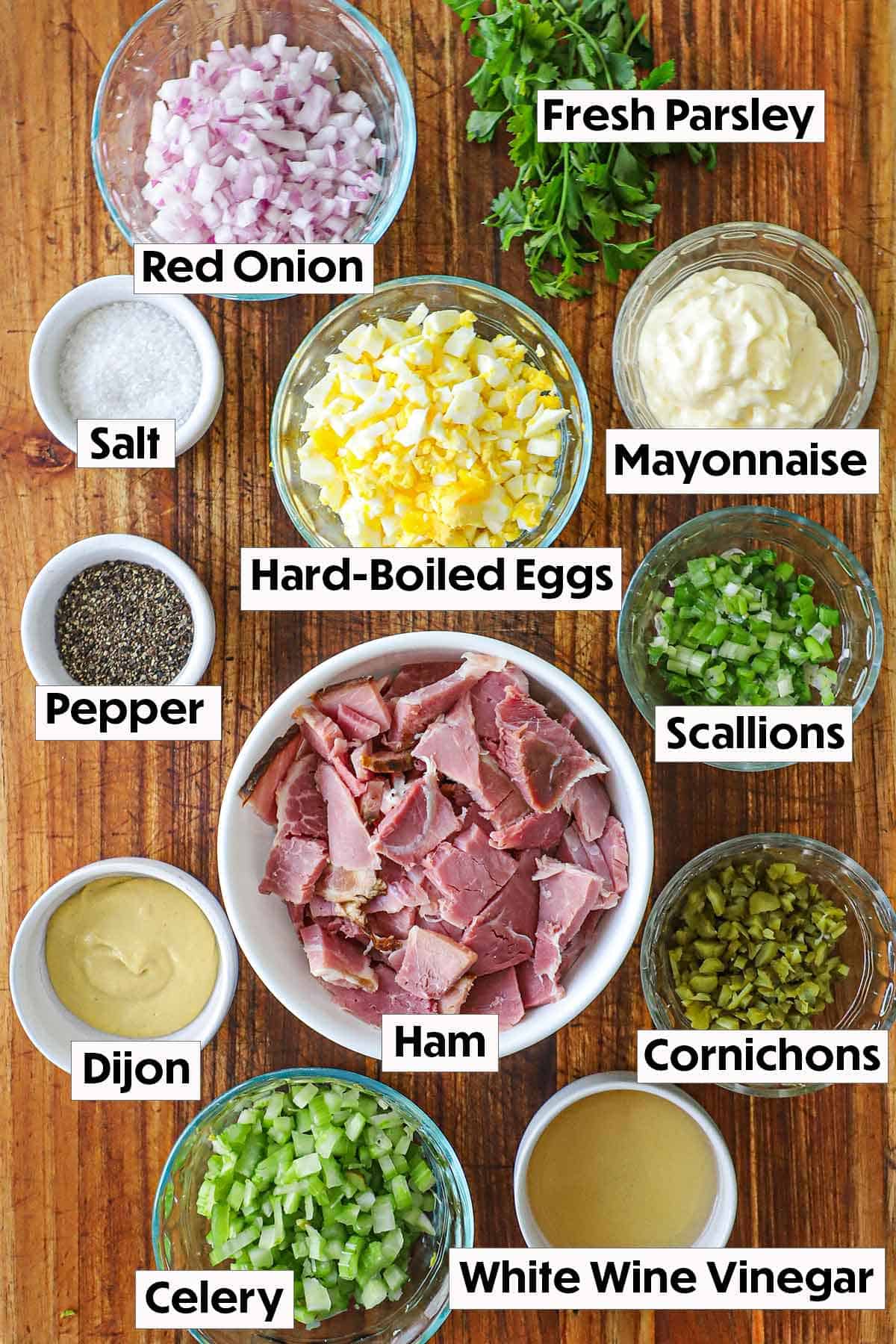 The ingredients for ham salad arranged on a wooden board, including chopped leftover ham, mayonnaise, mustard, chopped celery, diced onions, and seasonings, all neatly organized for easy preparation.