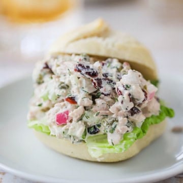 A slider sandwich stuffed with best-ever tuna salad and a piece of green leaf lettuce on a soft roll resting on a white lunch plate.