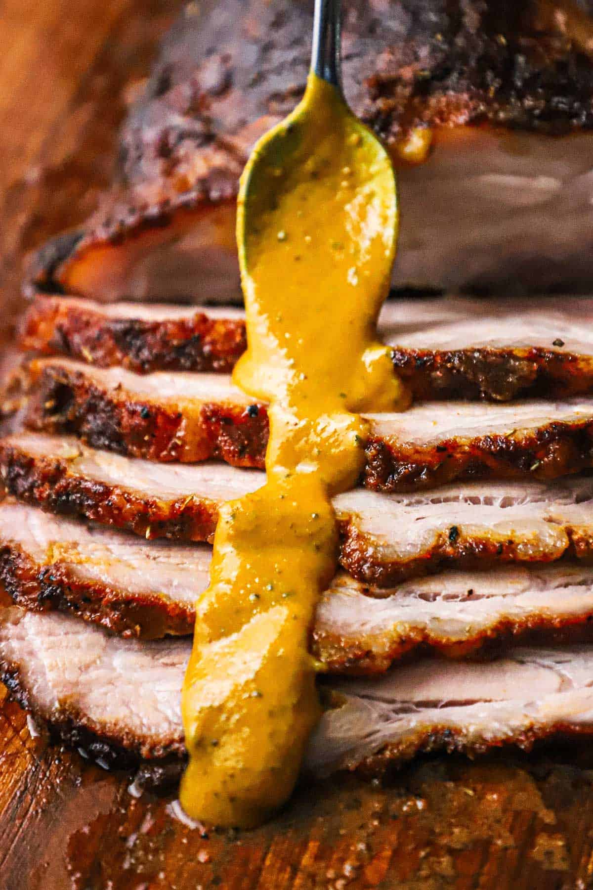 A person using a spoon to pour a line of Carolina mustard sauce over sliced pork brisket.