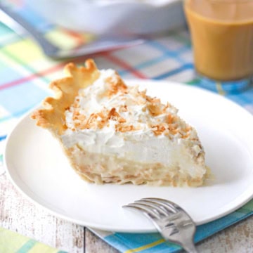 A slice of homemade coconut cream pie on a white dessert plate with the pie behind it.