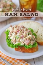 A white plate topped with a thick slice of white bread topped with a layer of green leaf lettuce and a serving of ham salad.