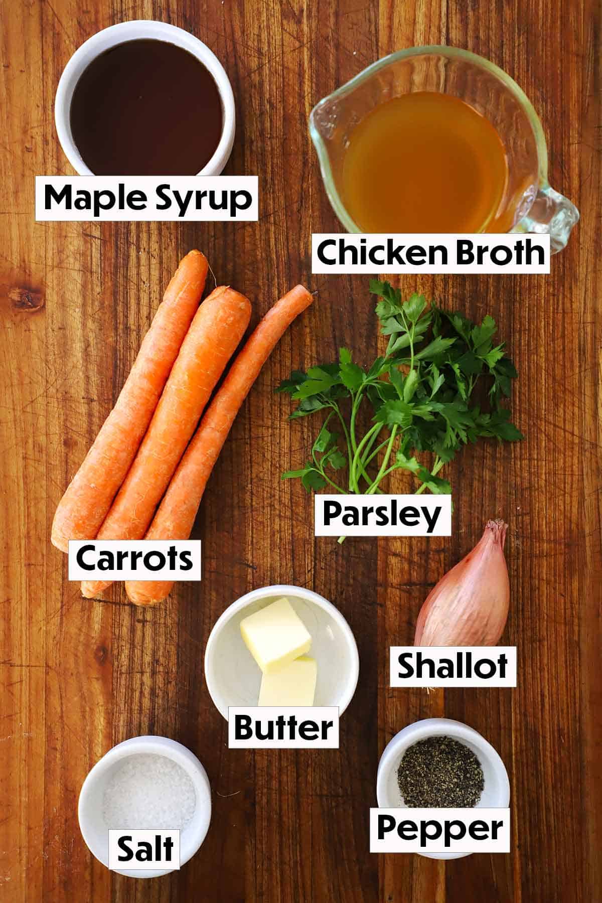 The ingredients for maple-glazed carrots displayed on a wooden background, including fresh carrots, maple syrup, butter, parsley, salt, and pepper, arranged neatly for easy preparation.