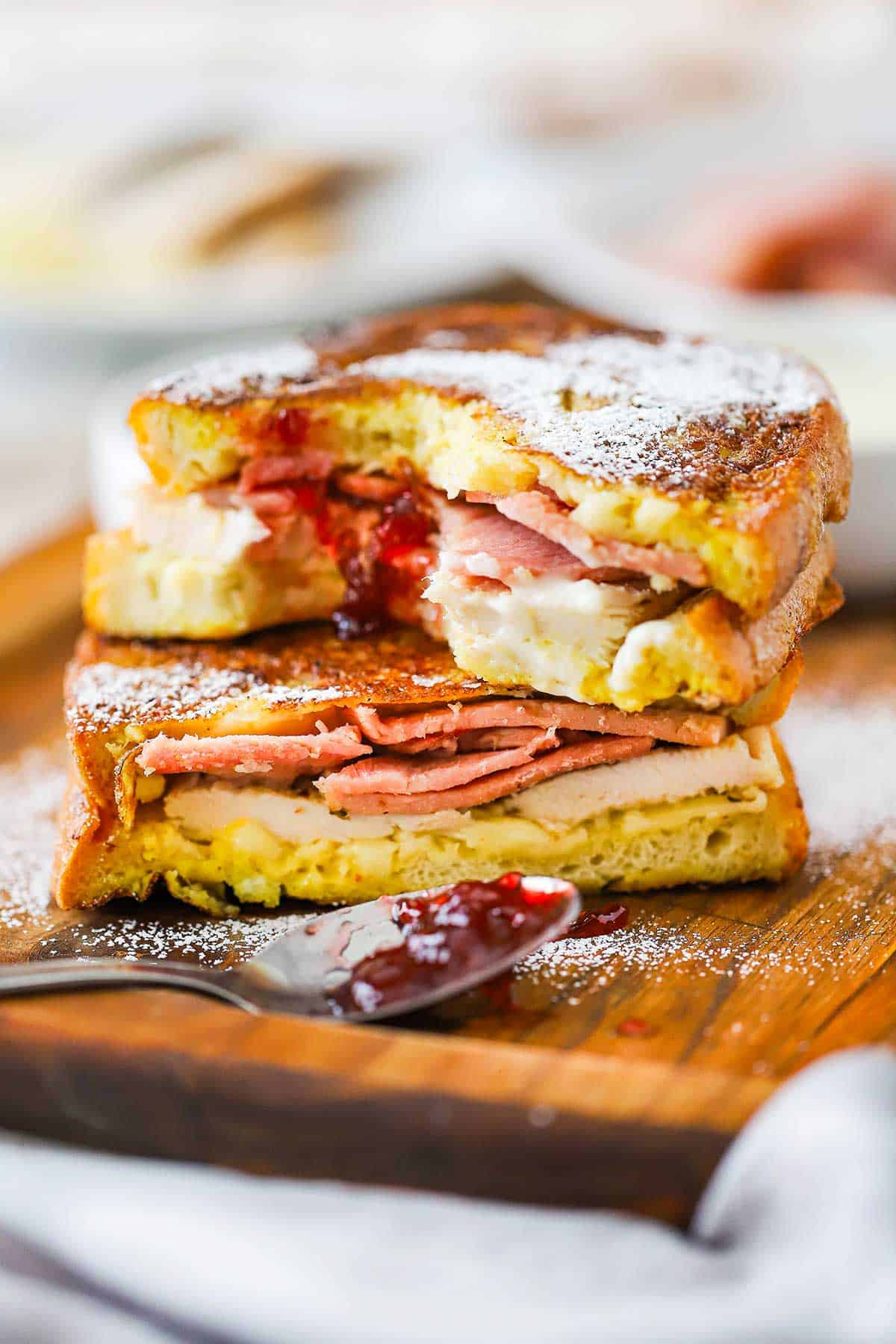 Two halves of a Monte Cristo sandwich one on top of the other on a small cutting board with powdered sugar sprinkled on top. 