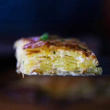 A square slice of layered potatoes dauphinoise being raised up on a large metal spatula.