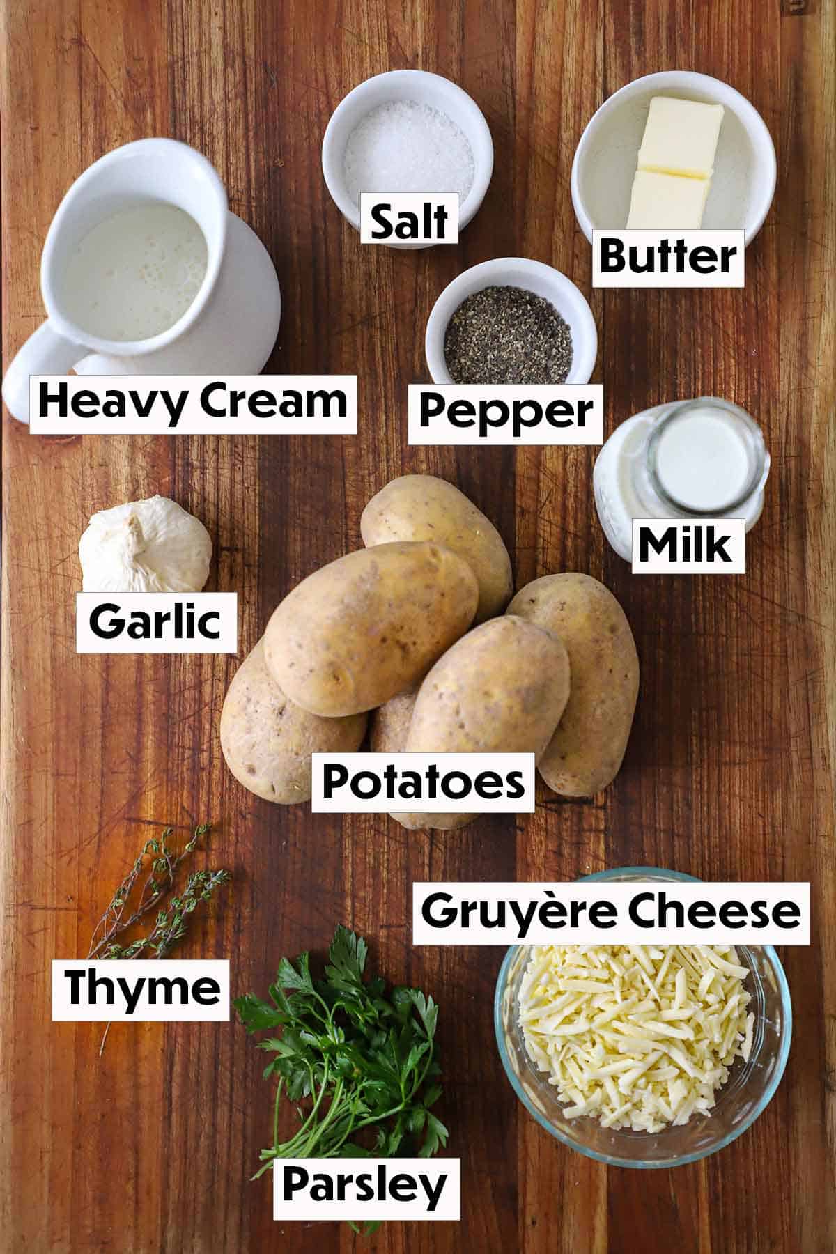 The ingredients for potatoes dauphinoise arranged on a wooden background, including thinly sliced potatoes, heavy cream, garlic, grated cheese, salt, and pepper, all neatly organized for easy preparation.