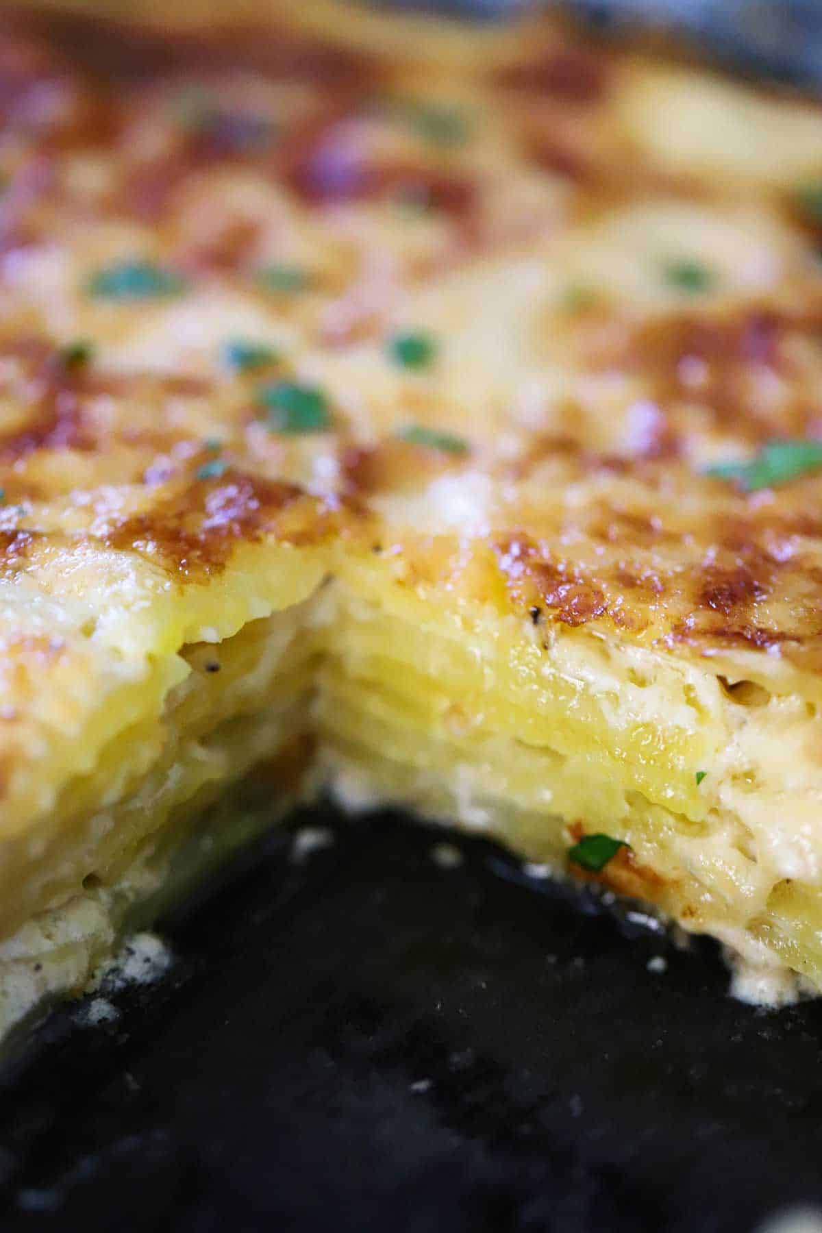 A baking dish filled with potatoes dauphinoise with a square piece missing from it. 