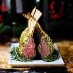 Roast rack of lamb persillade on a white platter with fresh rosemary along the base of the roast.