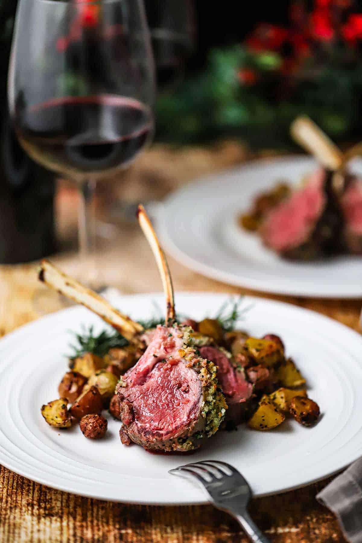 A white dinner plate filled with a serving of two French lamb chops with roasted potato wedges around the chops.