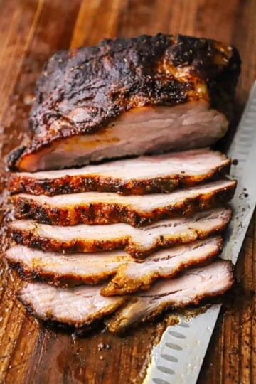 A sliced smoked brisket that is resting on cutting board with a large butcher's knife just underneath the meat.