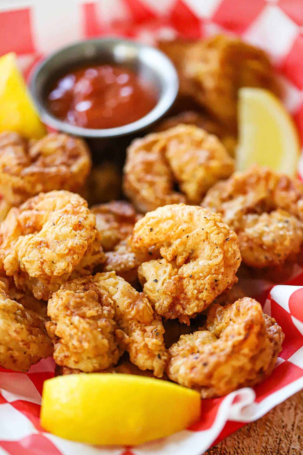 A basket lined with red and white checkered wax paper and filled with Southern-fried shrimp along with a lemon wedge and small bowl of cocktail sauce.