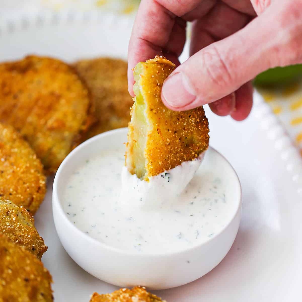 A person plunging half of a fried green tomato into a small white bowl filled with homemade Ranch dressing. 